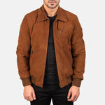 A man wearing a brown suede jacket over a black shirt and black pants, shown from the chin down against a light gray studio background.