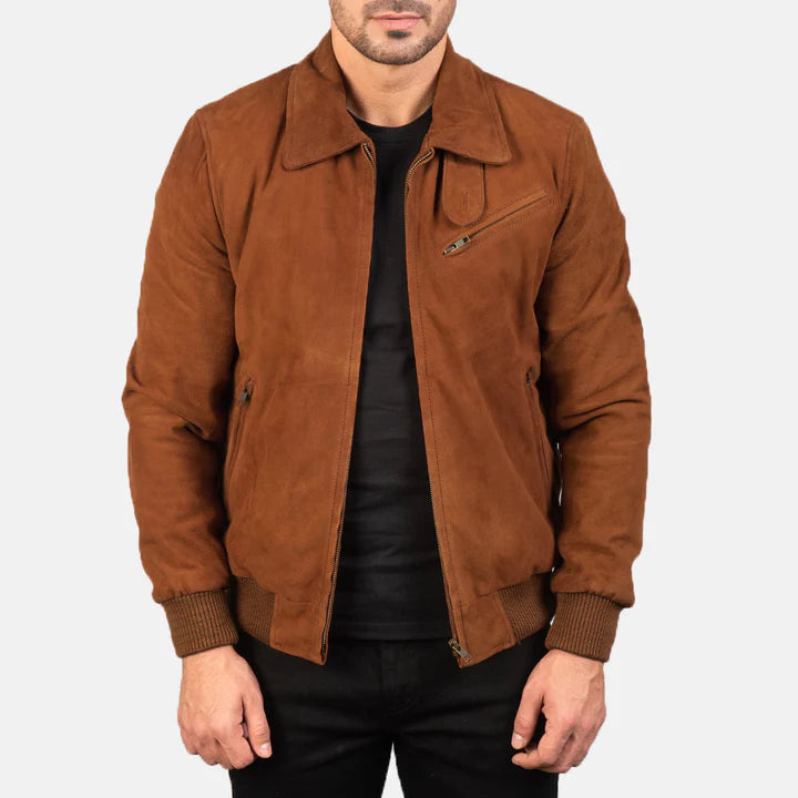 A man wearing a brown suede jacket over a black shirt and black pants, shown from the chin down against a light gray studio background.