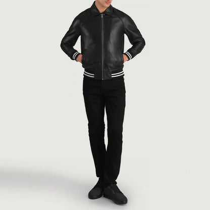 A man wearing a black leather bomber jacket with white stripes on the ribbed collar, cuffs, and hem, paired with black pants and black sneakers, set against a plain light gray studio background.