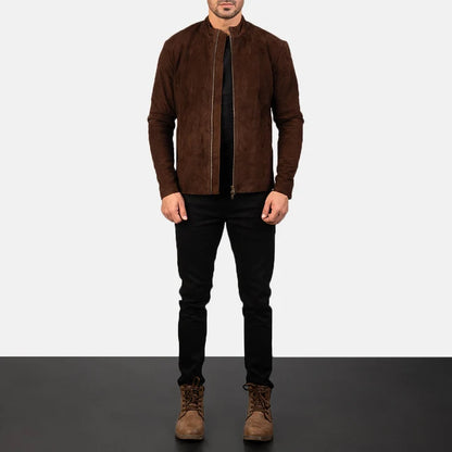 A man wearing a brown suede jacket, black pants, and brown boots, standing against a split white and dark gray studio background.