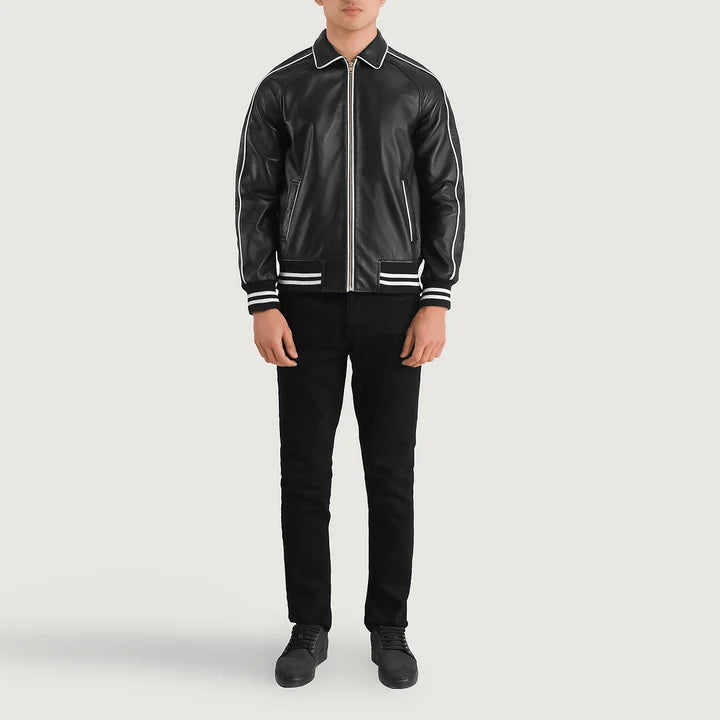 A model wearing a black leather varsity-style jacket with white contrast stitching and zippers, paired with black pants and black shoes, against a light gray studio background.