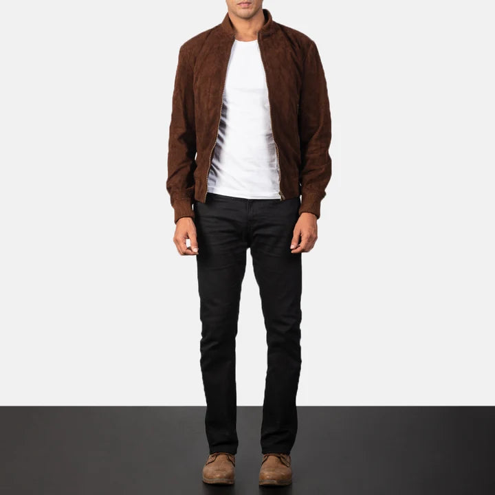 A man wearing a brown suede bomber jacket over a white t-shirt, black jeans, and brown suede shoes, standing against a split white and black studio background.