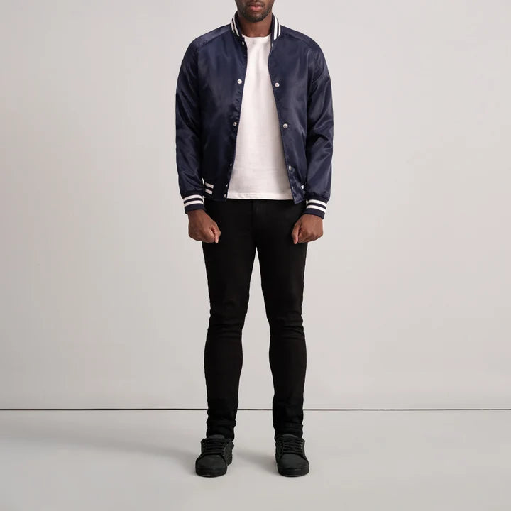 Person wearing a navy bomber jacket, white shirt, black pants, and black shoes on a light gray background