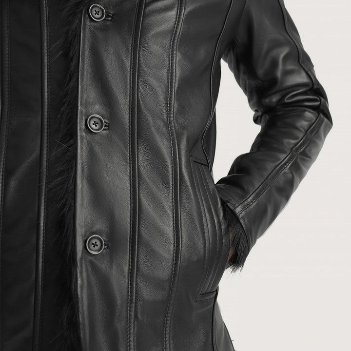 Close-up of a black leather jacket with vertical seam detailing, dark buttons, and a dark textured lining or fur trim, shown on a model against a light gray background.
