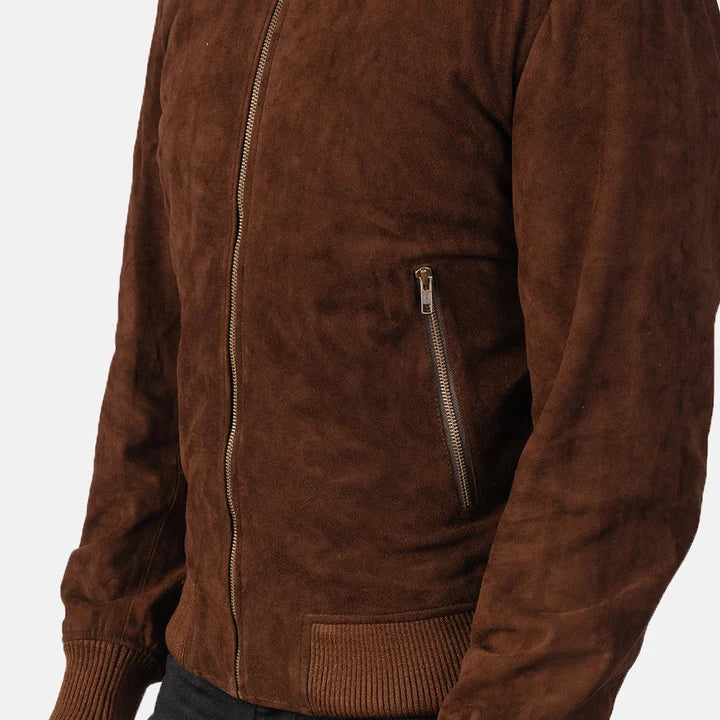 A close-up of a brown suede jacket with a front zipper, a zippered chest pocket, and ribbed cuffs and hem, shown on a model against a light gray background.